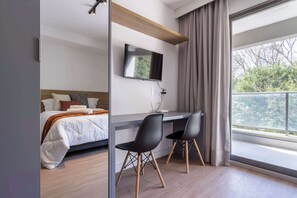 A hotel room with a bed, a desk with two chairs, a flat-screen TV, and a large window with curtains. - Studio Completo a 200m do Nubank Parque | AP3004 (Perdizes)