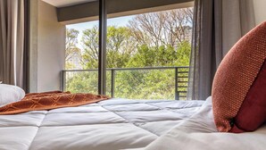 A bed with a white quilt, a brown knitted blanket, and a red pillow. - Studio Completo a 200m do Nubank Parque | AP3004 (Perdizes)