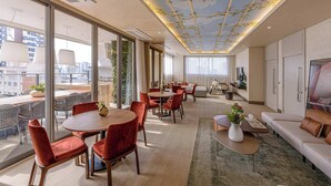 A modern hotel room with a dining area, a sofa, a TV, and a balcony with a city view. - Studio Completo a 200m do Nubank Parque | AP3004 (Perdizes)