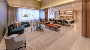 A modern living room with a sofa, armchair, coffee table, and dining area with chairs and a kitchen in the background. - Studio Completo a 200m do Nubank Parque | AP3004 (Perdizes)