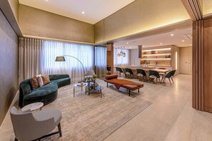 A modern living room with a sofa, armchair, coffee table, and dining area with chairs and a kitchen in the background. - Studio Completo a 200m do Nubank Parque | AP3004 (Perdizes)
