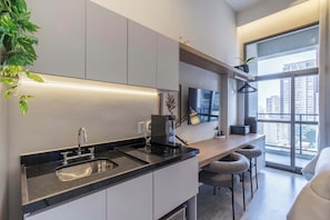 A modern kitchen with a built-in sink, a coffee machine, and a TV above the counter. - Studio Completo a 100m do Metrô Brooklin | HM1108 (Brooklin)