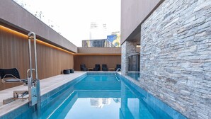 A modern indoor pool with a stone wall, a wooden panel wall, and a metal ladder. - Studio Completo a 100m do Metrô Brooklin | HM1108 (Brooklin)