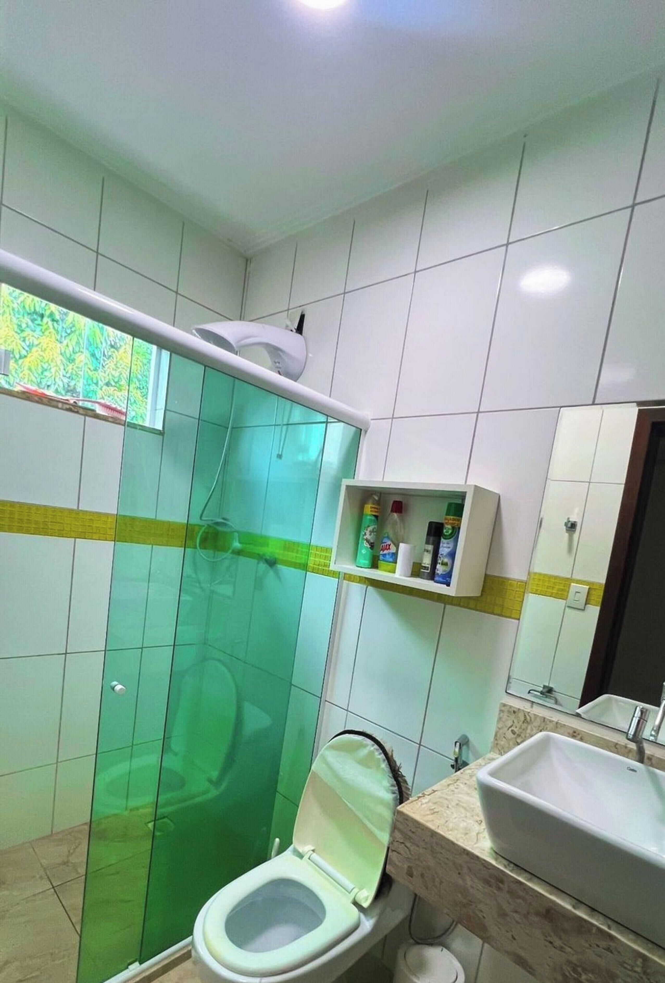 A bathroom with a glass shower enclosure, a toilet, a sink, and a shelf with toiletries.