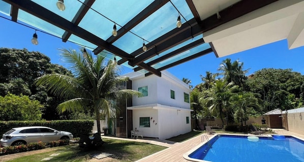 A modern two-story house with a swimming pool, a covered patio, and a car parked in the driveway. - Recanto Jacuípe Prime c Piscina Camaçari (Camaçari)