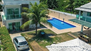 Ein modernes, zweistöckiges Gebäude mit Swimmingpool, umgeben von üppiger Bepflanzung und Palmen.