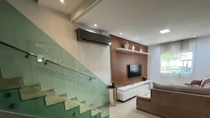Ein modernes Wohnzimmer mit Treppe, einem Flachbildfernseher, einer weißen Unterhaltungsanlage und einem beigen Sofa.