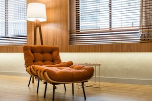 A modern room with a wooden floor, a tufted orange chair, a floor lamp, and large windows with blinds. - Flat no The World Vila Olímpia Cyclinn | #TW1508 (Itaim Bibi)