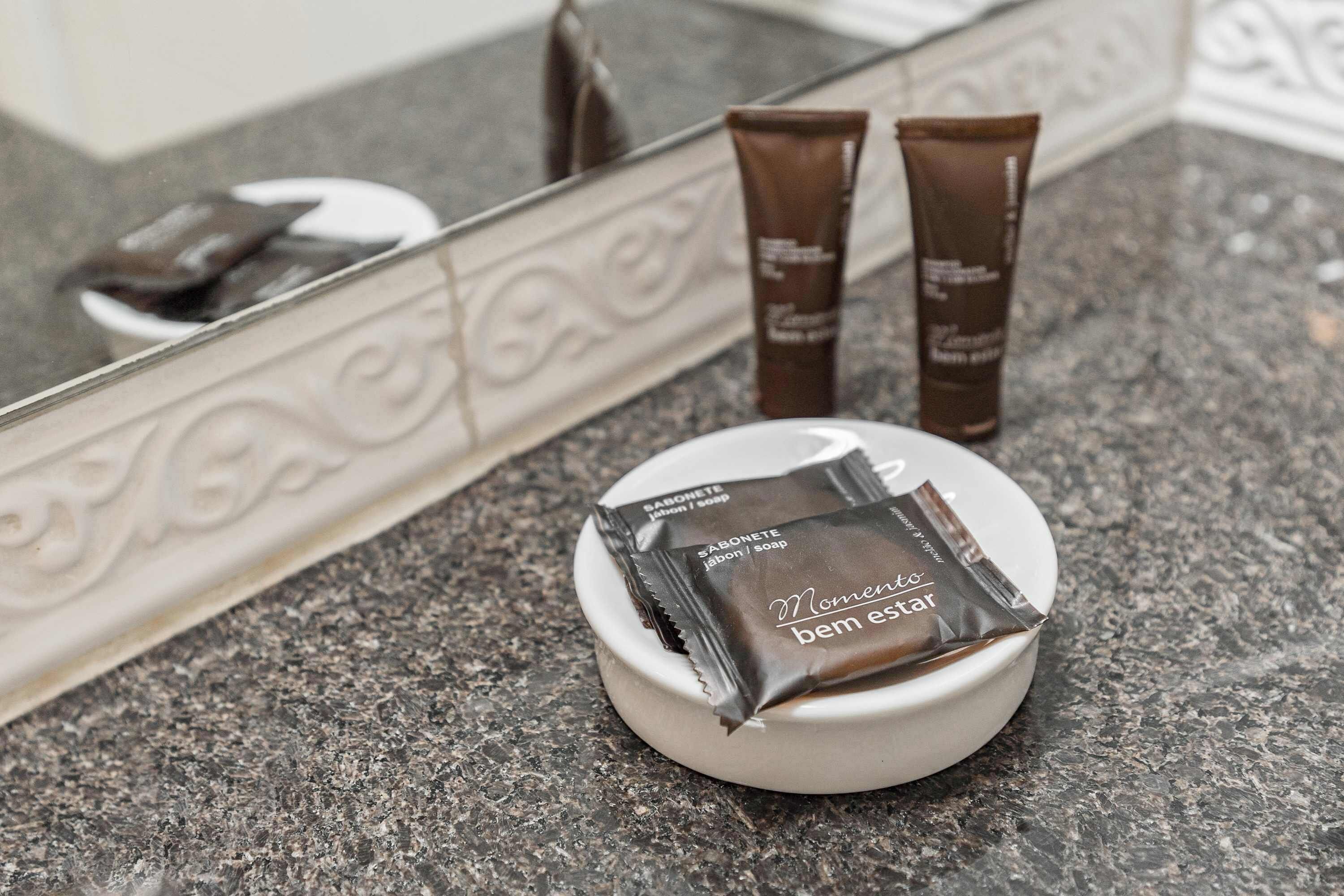 Une salle de bain avec un comptoir en marbre, un lavabo blanc et deux tubes de produits de toilette marron.