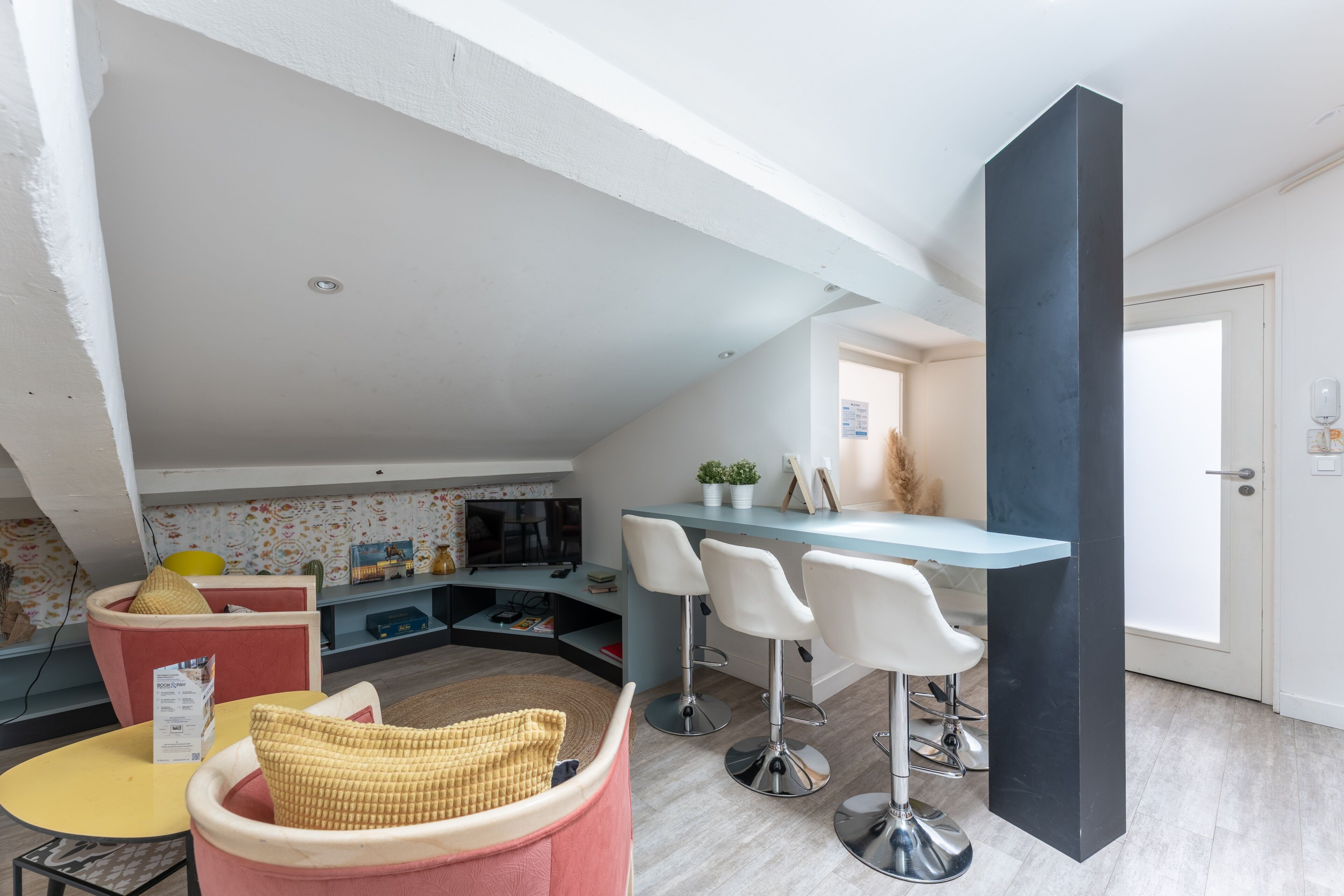 A modern kitchen with a bar area, a dining table with chairs, and a cozy seating area with cushions.