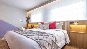 Una cama bien hecha con cubrecolcha acolchado, una mesita de noche con lámpara, y una lámpara de pared.