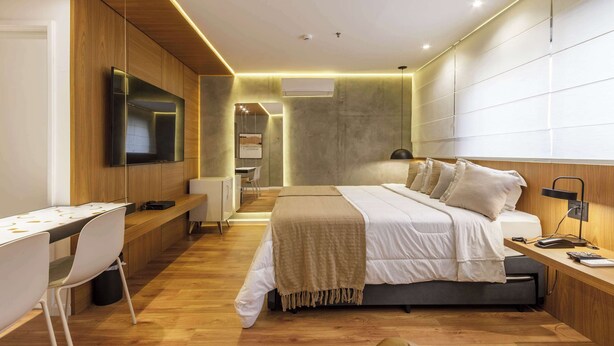 A modern bedroom with a bed, bedside table, desk, chair, and a TV mounted on the wall. - Cyclinn a 500m da Faria Lima | #TR502 (Itaim Bibi)