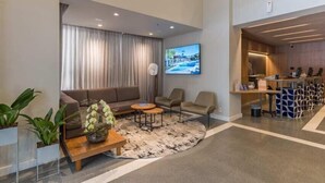 A modern hotel lobby with a sofa, chairs, a coffee table, a TV, and a reception desk. - Cyclinn a 500m da Faria Lima | #TR502 (Itaim Bibi)