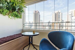 Een balkon met een gewatteerd bankje, een klein rond tafeltje met een kopje en een blauwe stoel.