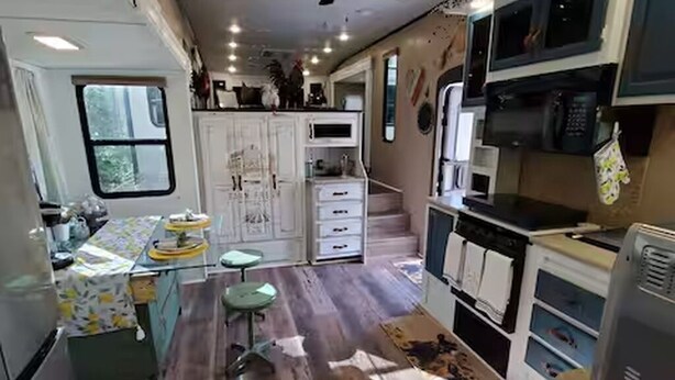Eine kleine Küche mit Kühlschrank, Mikrowelle und Herd. Ein Fenster und ein kleiner Hocker sind vorhanden.