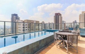 Une piscine sur le toit offrant une vue sur les bâtiments de la ville, des meubles d’extérieur et un ciel dégagé.