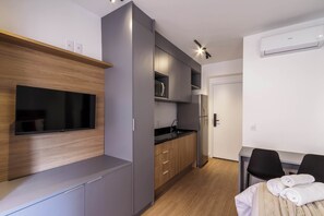 Une cuisine moderne équipée d’un téléviseur à écran plat, d’un four à micro-ondes encastré et d’un réfrigérateur. Un coin repas avec une table et des chaises est à votre disposition, ainsi qu’un lit avec des serviettes.