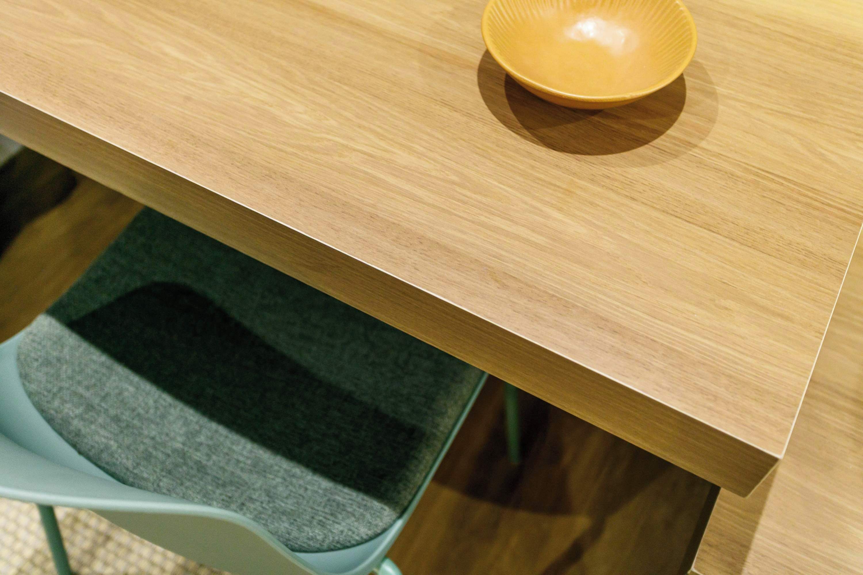 A wooden table with a bowl on it, a grey chair, and a carpeted floor.