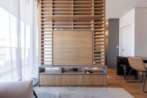 Quarto moderno com TV integrada, estantes de madeira, escrivaninha e cadeira.