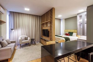 Quarto de hotel moderno com sofá, mesa de jantar, televisão, cama e guarda-roupa.
