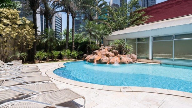 Una piscina con lettini, palme e una roccia decorativa.