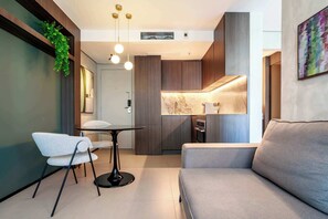 Ein modernes Interieur mit einer Couch, einem Esstisch und Stühlen, einer Küchenzeile mit Marmorarbeitsplatte und einer hängenden Pflanze.
