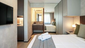 Una camera d'albergo con un letto, una televisione, un bagno con lavandino e specchio, e un comodino con una lampada.