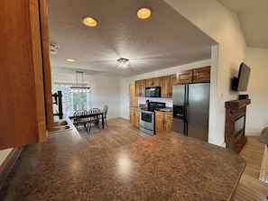 A kitchen with wooden cabinets, a stainless steel refrigerator, a microwave, and a dining area with chairs.