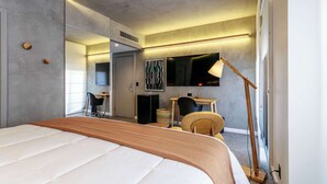 Una camera d'albergo moderna con un letto grande, una scrivania, una sedia, una lampada e una grande finestra.