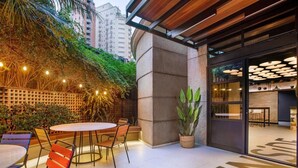 Patio esterno con tavolo e sedie rotonde, una pianta in vaso e l'ingresso di un edificio con porta in vetro.