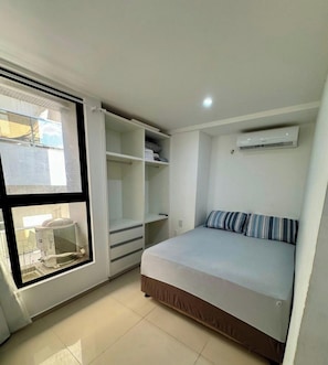 A bedroom with a bed, a window, a wardrobe, and an air conditioning unit.
