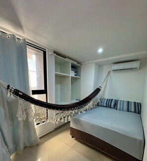 A room with a hammock, a bed, a wardrobe, and an air conditioning unit. - Flat Santorini com Piscina - João Pessoa (João Pessoa)