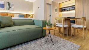 Ein modernes Wohnzimmer mit einer Couch, einem kleinen runden Tisch mit einer Pflanze sowie einem Essbereich mit Stühlen und einem Holztisch.