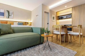 A modern living room with a sofa, a small round table with a plant, and a dining area with chairs and a wooden table. - #EB904 | Cyclinn Brooklin Santo Amaro (Brooklin)