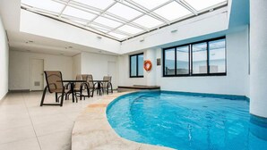 Ein Hallenbad mit Glasdach, einem Rettungsring und einem Tisch mit Stühlen.