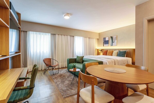 Une chambre d’hôtel comprenant un lit, une table à manger, un canapé, une chaise et une petite table avec une plante.