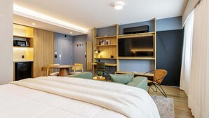 Ein modernes Hotelzimmer mit einem Bett, einem Schreibtisch, einem Sessel, einem Fernseher und einem Regal mit Büchern und einer Lampe.