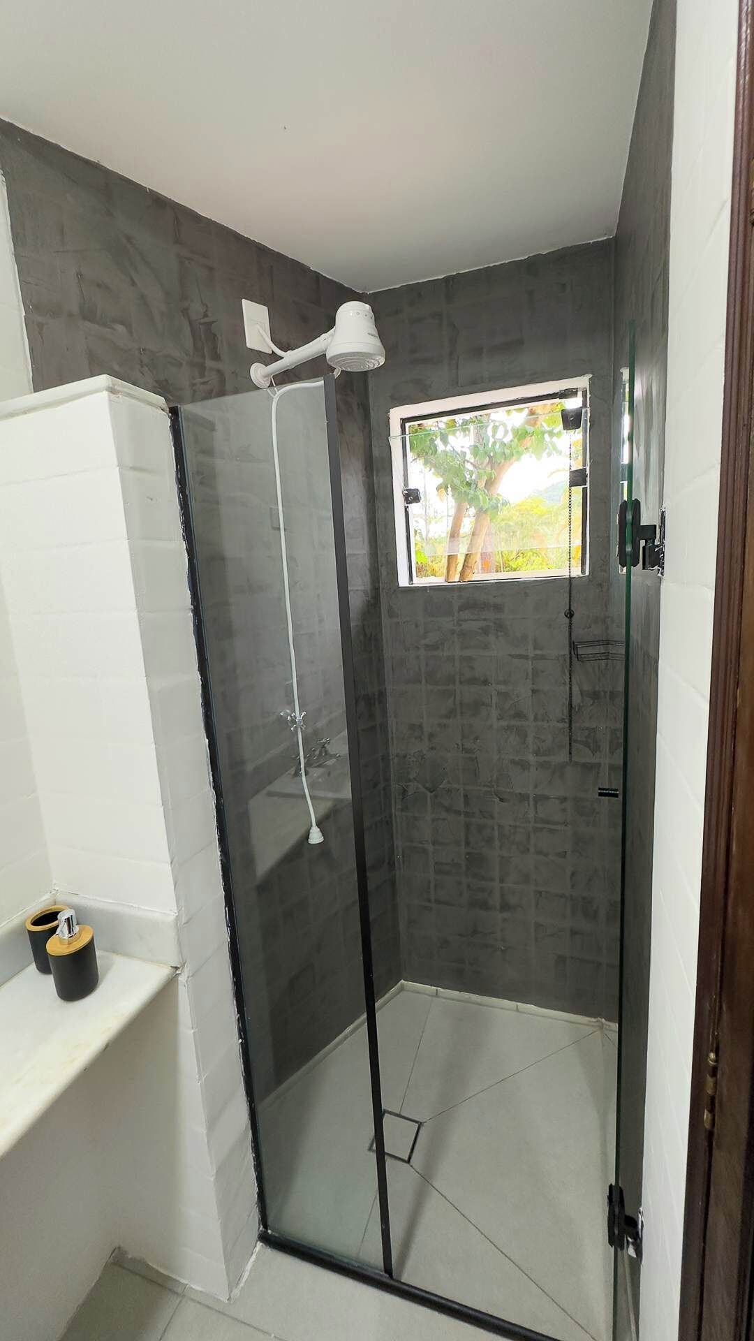 Une douche avec une porte en verre, une petite fenêtre et un plafonnier blanc.