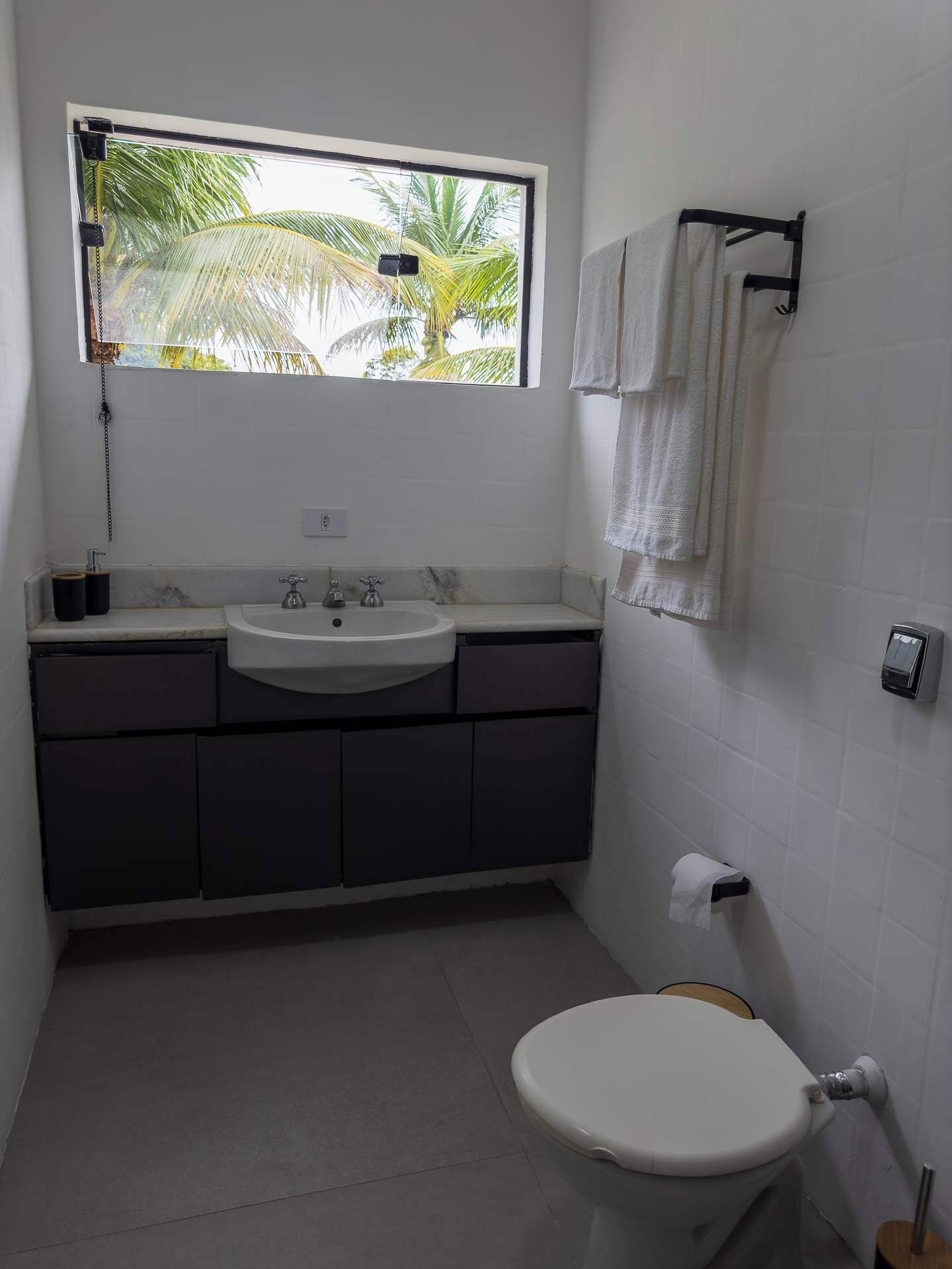 A bathroom with a window, a sink, a toilet, and a towel rack.
