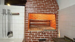 Un four extérieur en briques, doté d’une grille métallique à l’intérieur, et entouré de murs recouverts de carreaux blancs.
