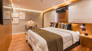 Ein modernes Schlafzimmer mit einem großen Bett, Nachttischen, einer Wand-Klimaanlage und einem kleinen Tisch mit Lampe.
