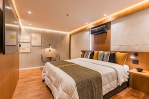 Ein modernes Schlafzimmer mit einem großen Bett, Nachttischen, einer Wand-Klimaanlage und einem kleinen Tisch mit Lampe.