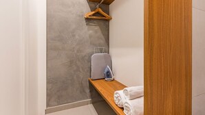 Ein Badezimmer mit einer grauen, strukturierten Wand, einem Holzregal mit Handtüchern, einer Kleiderstange und einem grauen Koffer.