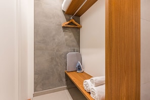 Ein Badezimmer mit einer grauen, strukturierten Wand, einem Holzregal mit Handtüchern, einer Kleiderstange und einem grauen Koffer.