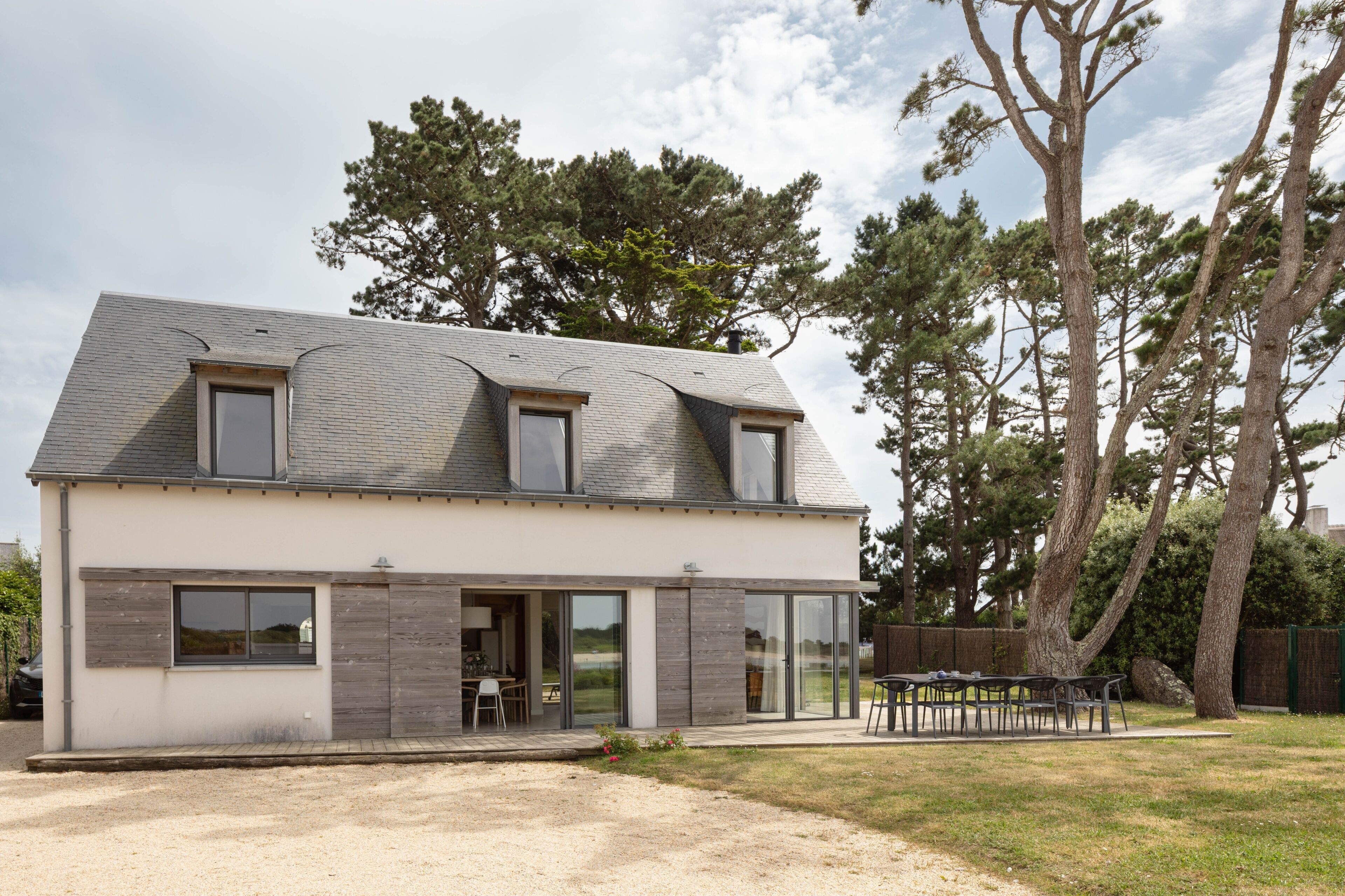 A modern two-story house with a sloped roof, large windows, and a patio area.