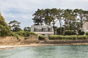 A coastal house with a stone wall, a staircase leading to the entrance, and a view of the sea. - Villa La Trinité Océan - Accès direct à la plage (La Trinite-sur-Mer)