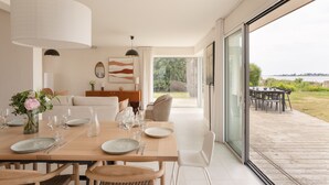 A dining area with a table set for six, a vase of flowers, and a view of the outdoors. - Villa La Trinité Océan - Accès direct à la plage (La Trinite-sur-Mer)