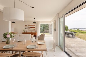 A dining area with a table set for six, a vase of flowers, and a view of the outdoors. - Villa La Trinité Océan - Accès direct à la plage (La Trinite-sur-Mer)