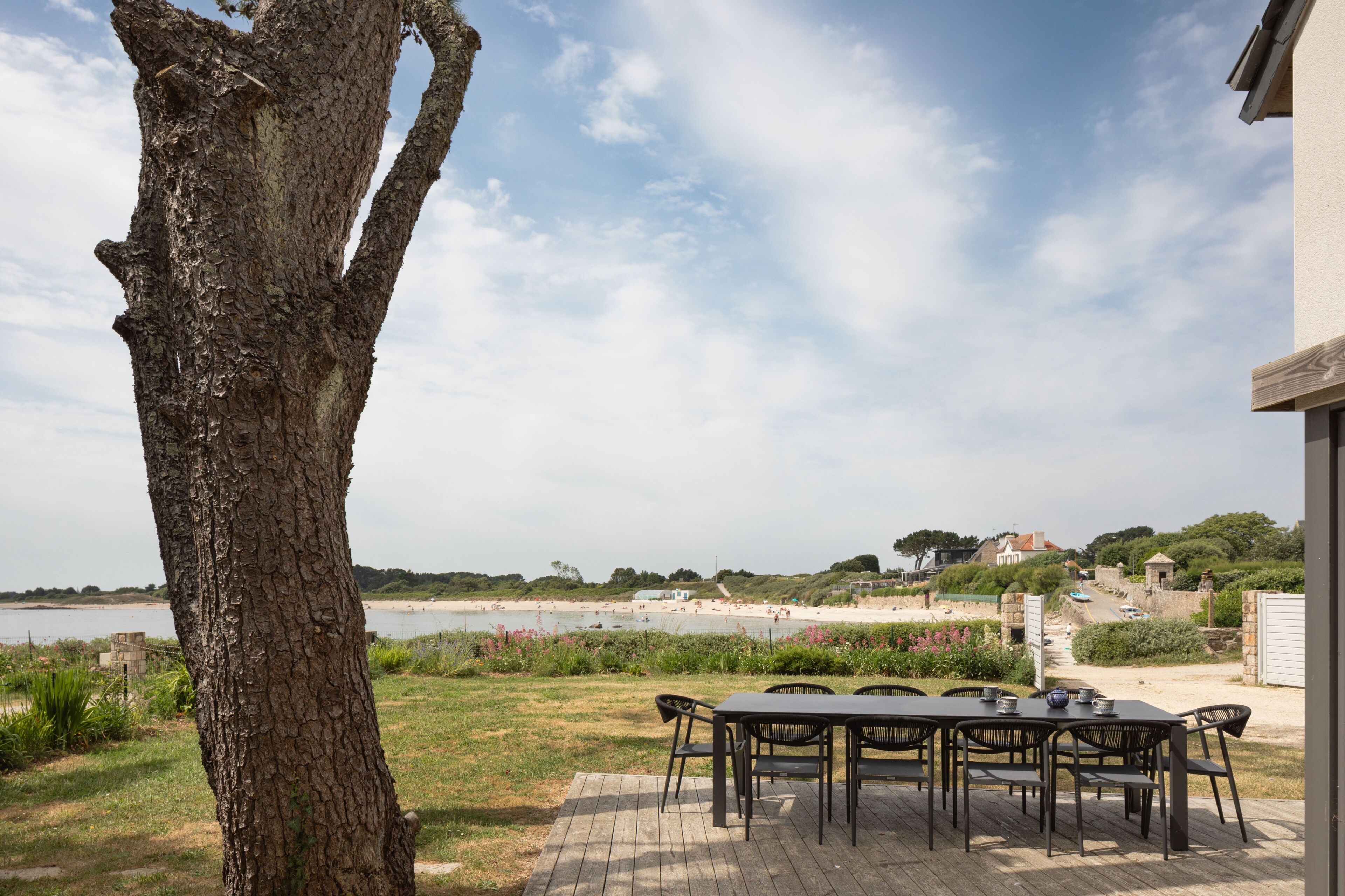Een terras met een tafel en stoelen, met uitzicht op een strand en het water.
