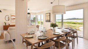A dining area with a large table set for six, a view of the outdoors, and a modern interior design. - Villa La Trinité Océan - Accès direct à la plage (La Trinite-sur-Mer)